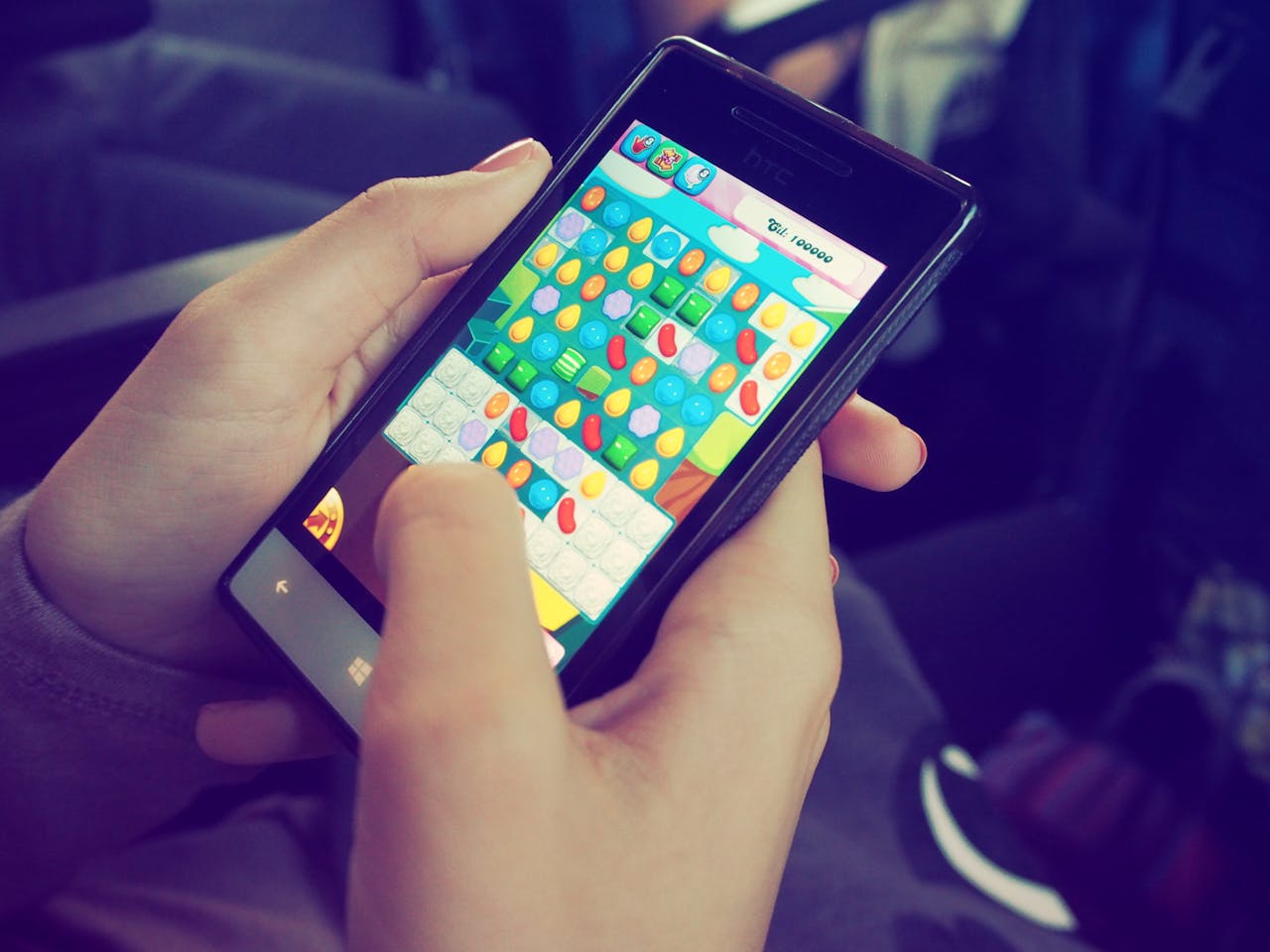 Hands holding a smartphone with a colorful puzzle game on the screen, displaying modern technology.